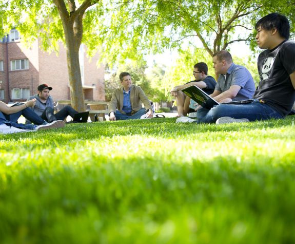 students sitting on campus lawn with professor